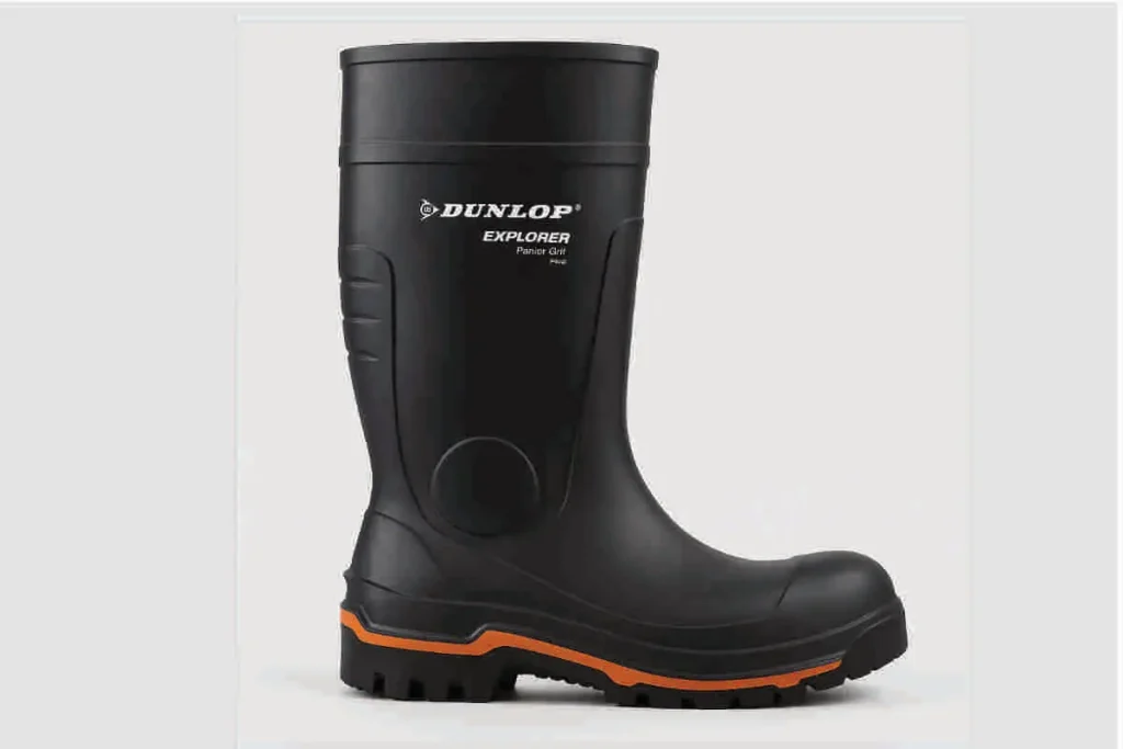Bota de goma Dunlop Explorer con punta de acero, color negro con suela naranja, vista lateral sobre fondo claro, ideal para trabajo en condiciones húmedas y exigentes.