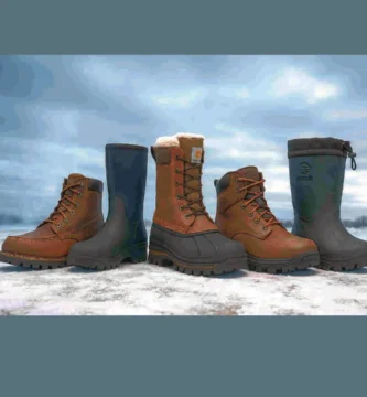 Cinco botas de trabajo para invierno alineadas sobre nieve, mostrando distintos estilos y materiales como cuero, neopreno y goma, bajo un cielo nublado.